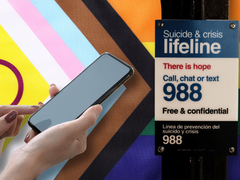 An advertisement for the 988 hotline is in the foreground with a person holding a phone. A Pride flag is in the background.
