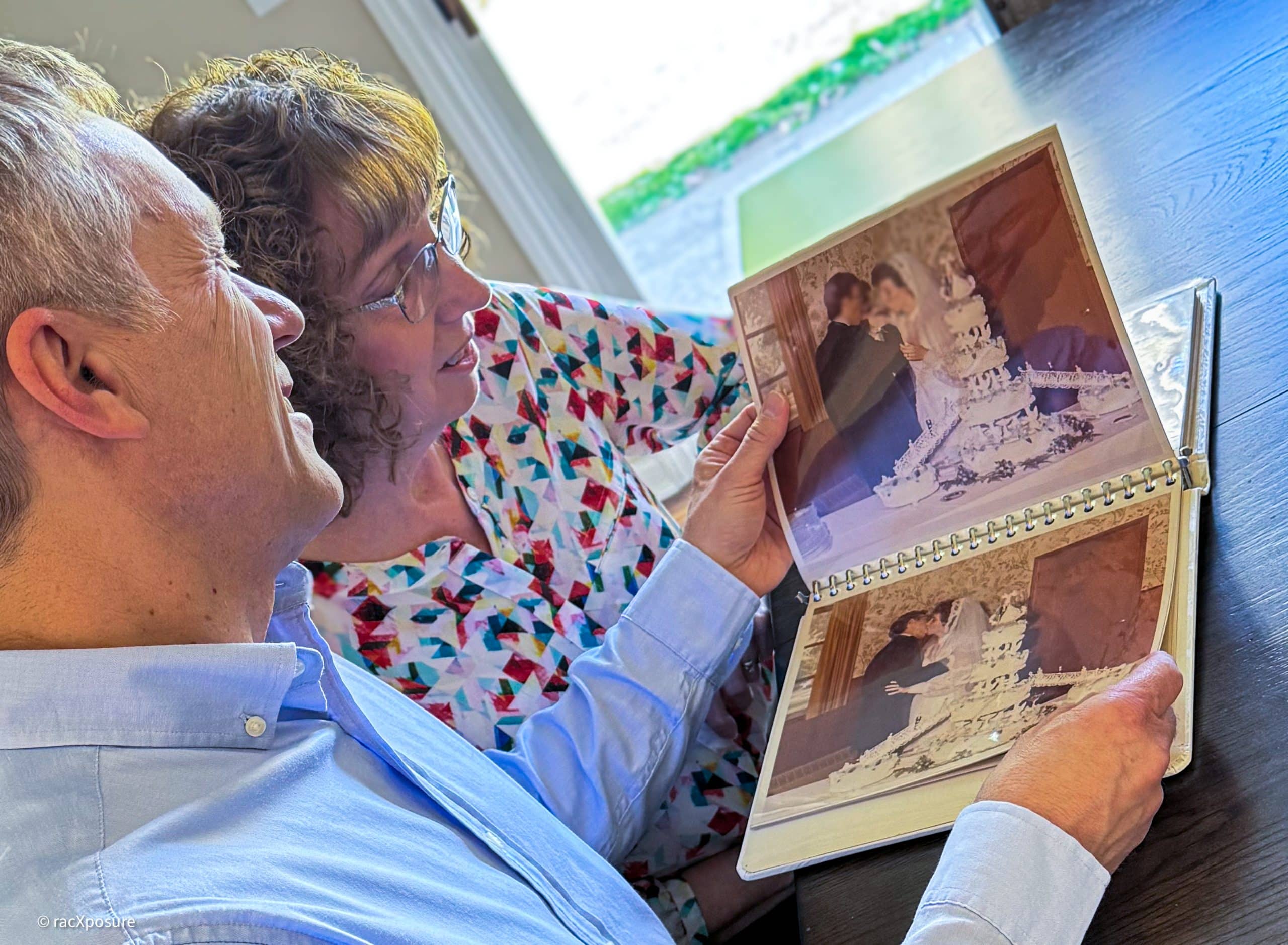 A husband and wife sit down at a kitchen table and flip through their marriage album.