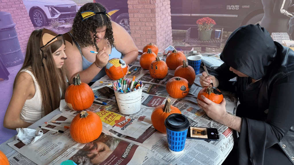 A photo of people painting pumpkins at a park's gazebo with a rainbow filter in the background.