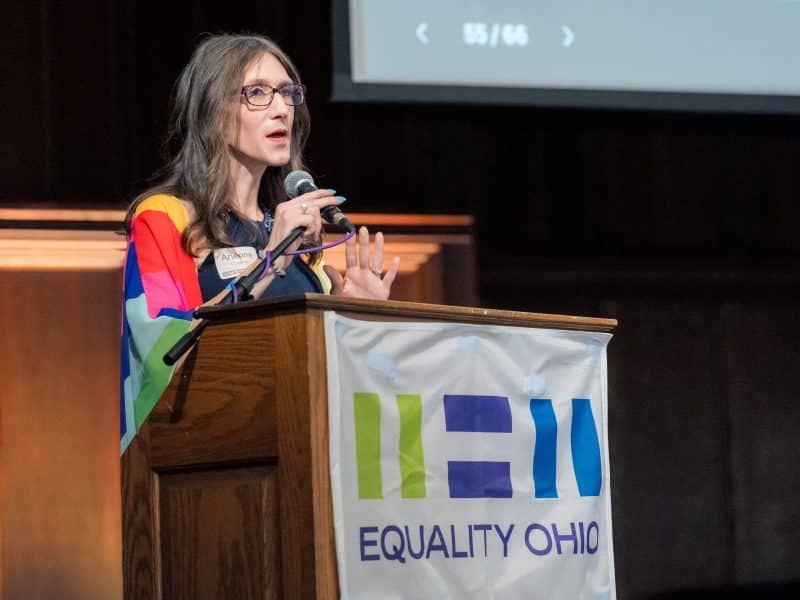 Transgender candidate for the Ohio statehouse Arienne Childrey speaks at a podium with an Equality Ohio banner draped in front.