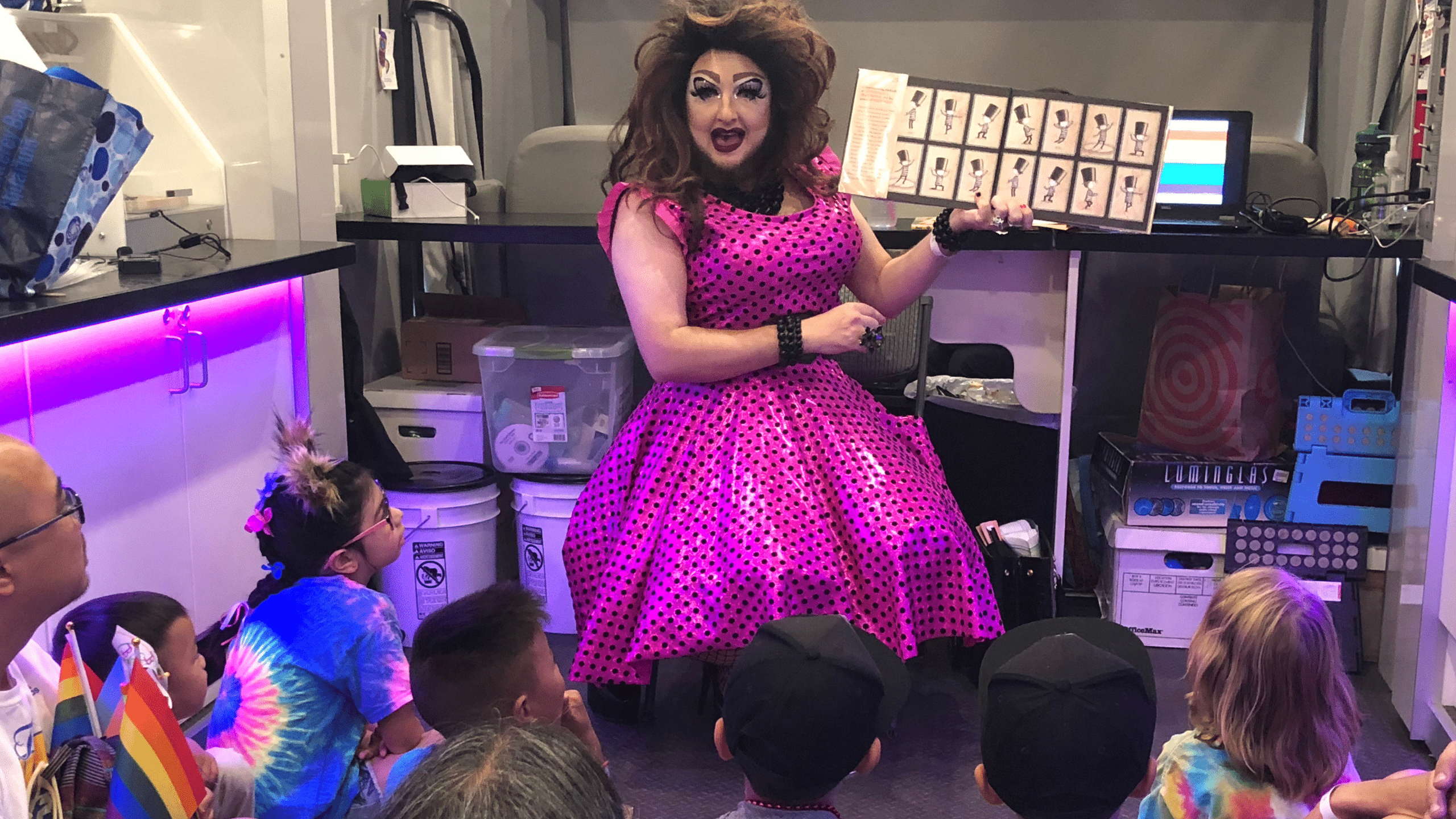 Drag queen reads a children's book to a group of children in a library.