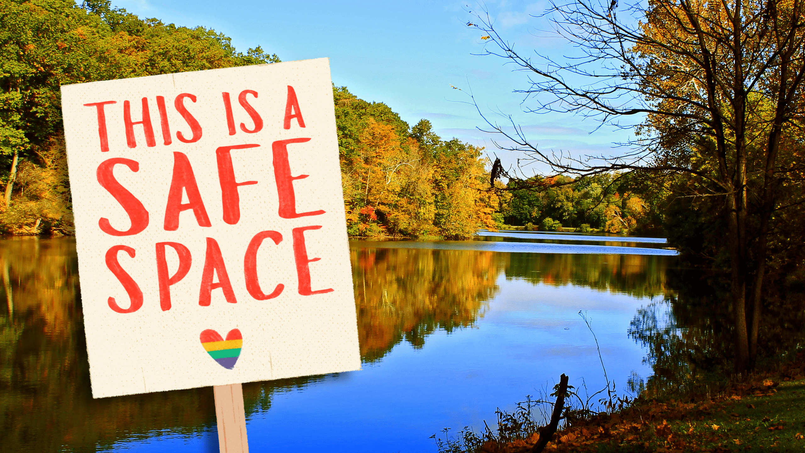 A sign is tilted as if on the bank of Glacier Lake in Youngstown, Ohio. The sign reads, "This is a safe space." A rainbow heart is underneath the lettering.