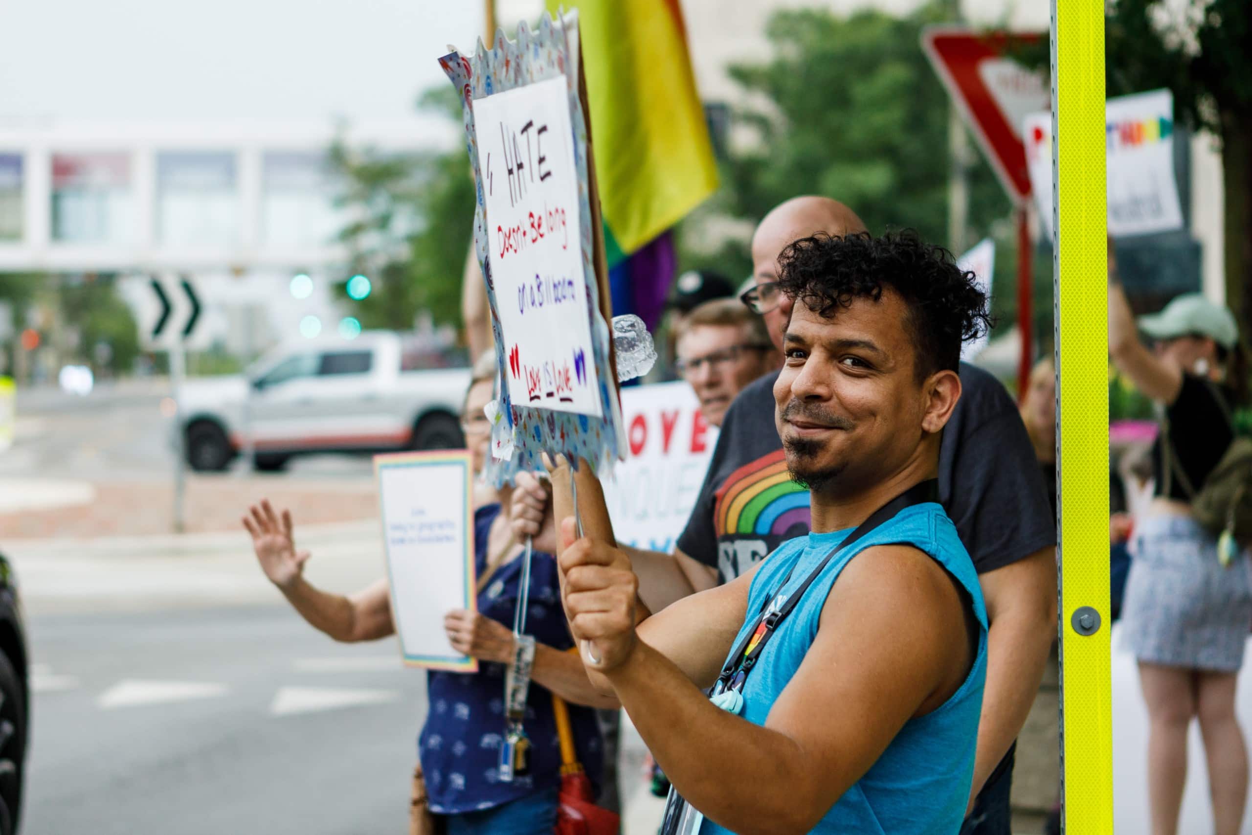 A man stands in a line of people holding a pro-LGBTQ+ sign at a rally.