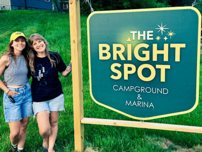 Tessa and Chelsea Pratt-Smith pose in front of the sign for their queer-friendly business called The Bright Spot Campground and Marina.