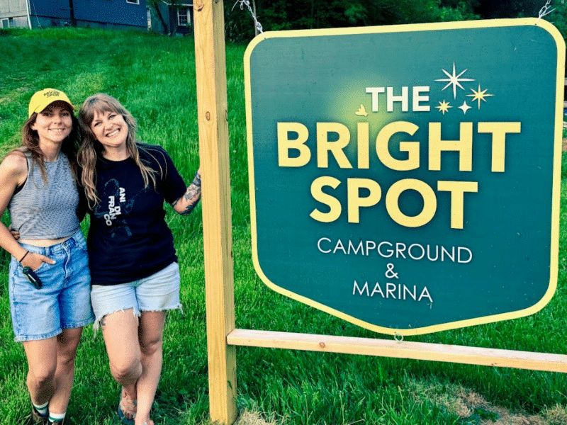 Tessa and Chelsea Pratt-Smith pose in front of the sign for their queer-friendly business called The Bright Spot Campground and Marina.